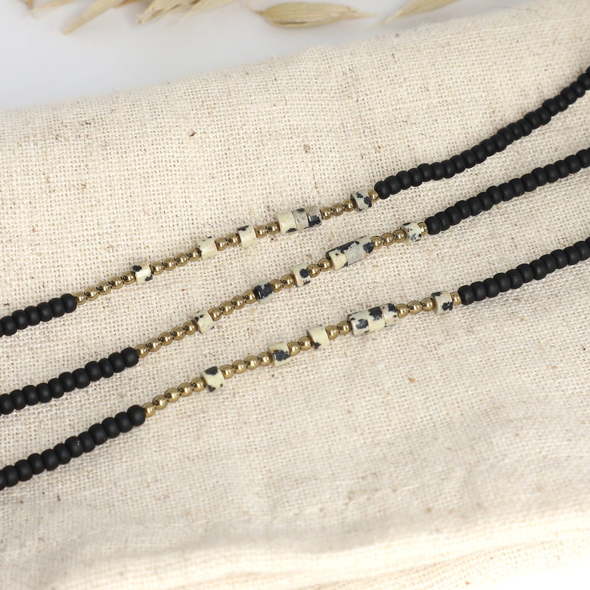 Drei Morsecode Armbänder Selflove aus schwarzen, goldenen und beigen Perlen auf Stoffunterlage