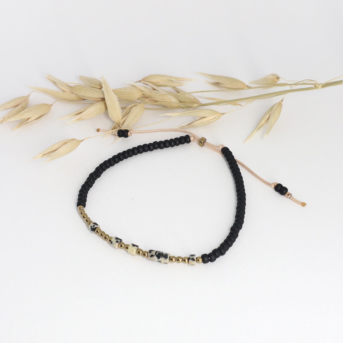 Minimalistisches Morsecode Armband Selflove mit schwarzen und goldenen Perlen neben getrockneten Halmen