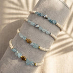 Vier größenverstellbare Aquamarin Armbänder auf einer Schmuckrolle mit Perlen und der Blume des Lebens in Gold und Silber.