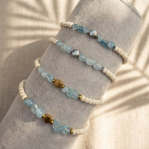 Vier größenverstellbare Aquamarin Armbänder auf einer Schmuckrolle mit Perlen und der Blume des Lebens in Gold und Silber.