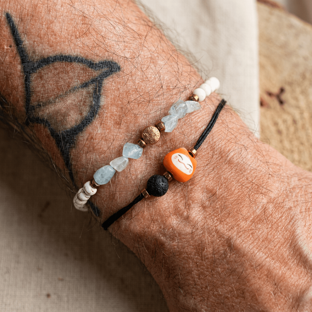 Makro-Produktfoto eines Aquamarin Armbands mit Blume des Lebens, kombiniert mit einem feinen schwarzen Band samt Lava-Perle an einem tätowierten Handgelenk.