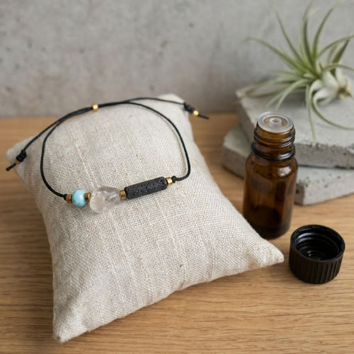 Ästhetisch inszeniertes Aromatherapie Armband mit Edelsteinen auf einem Kissen, im Hintergrund eine minimalistische Pflanze.