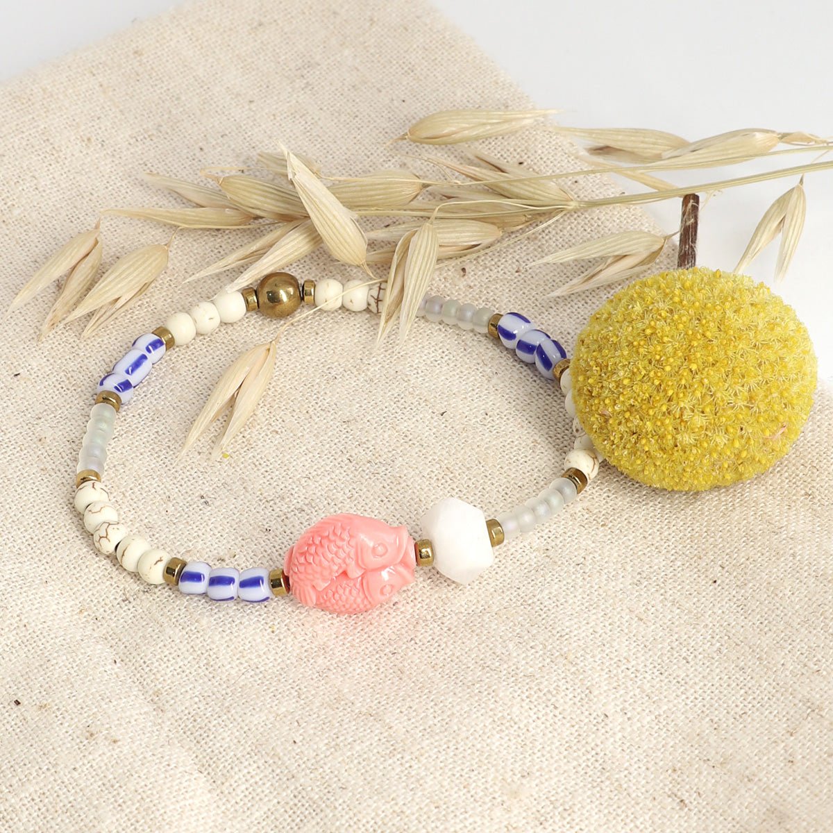 Boho-Armband mit rosa Fischanhänger und gelber Blüte auf Leinenstoff