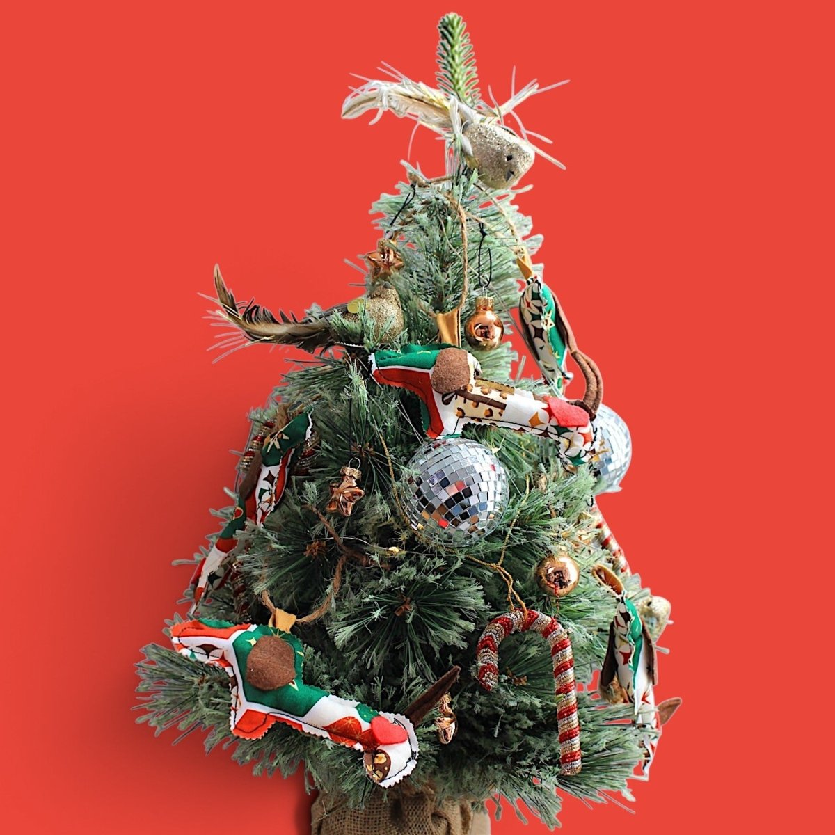 Kleiner Weihnachtsbaum vor rotem Hintergrund, dekoriert mit handgemachten Dackel-Anhängern aus Stoff.