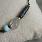 Nahaufnahme eines eleganten Diffuser Armbands mit hellblauem Larimar, klarem Rutilquarz und schwarzem Lavastein auf einem Leinenkissen.