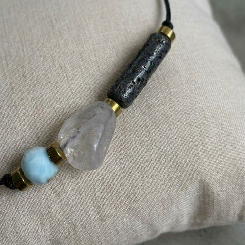 Nahaufnahme eines eleganten Diffuser Armbands mit hellblauem Larimar, klarem Rutilquarz und schwarzem Lavastein auf einem Leinenkissen.