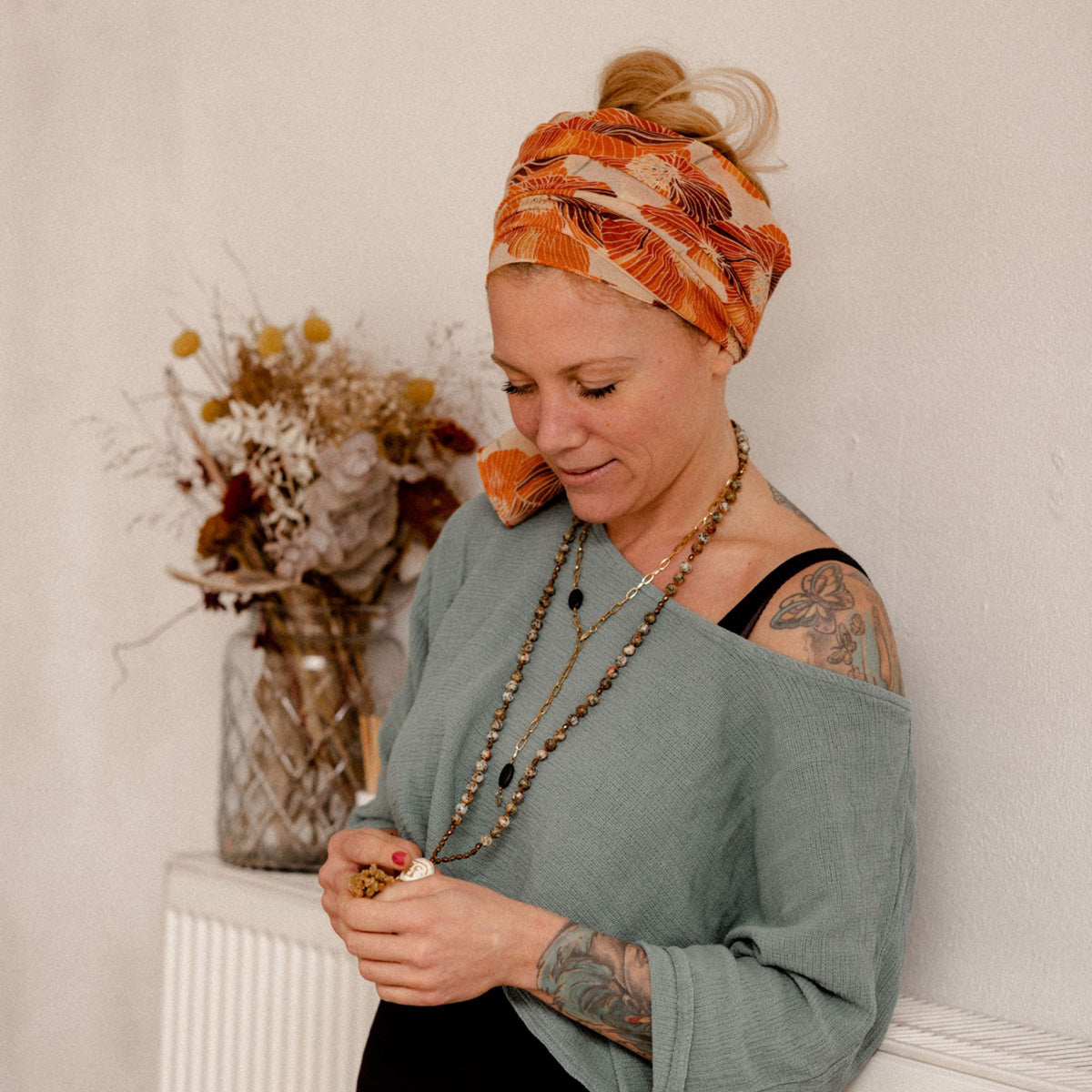 Frau mit Turban und Tattoos trägt handgefertigte Mala-Kette und schaut nach unten