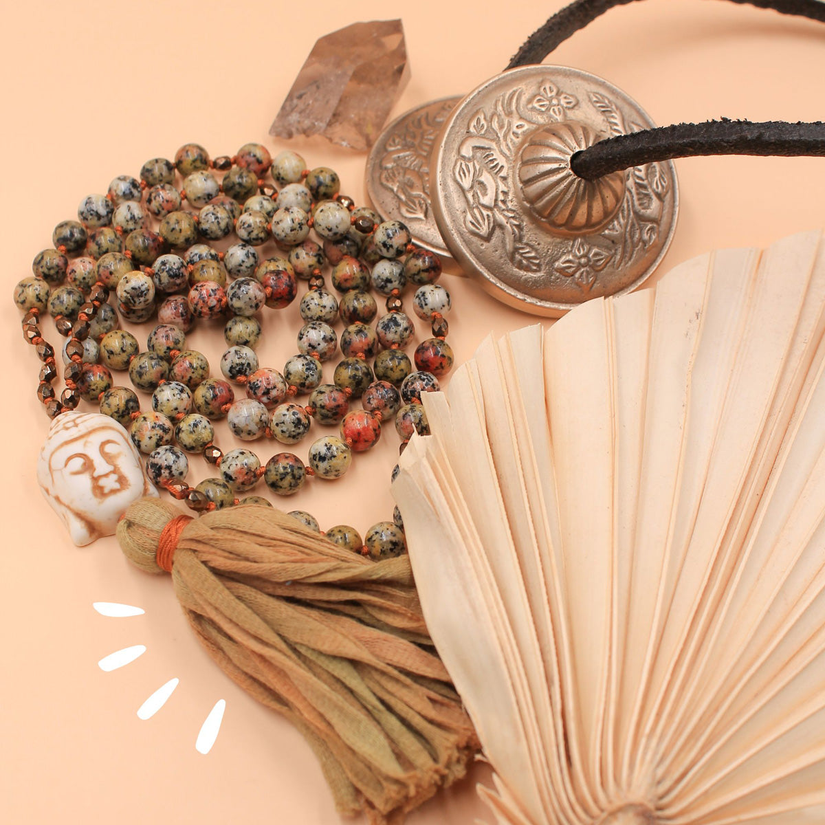 Bunte Mala-Kette mit Buddha-Anhänger und Quaste liegt als Flatlay mit Dekoobjekten