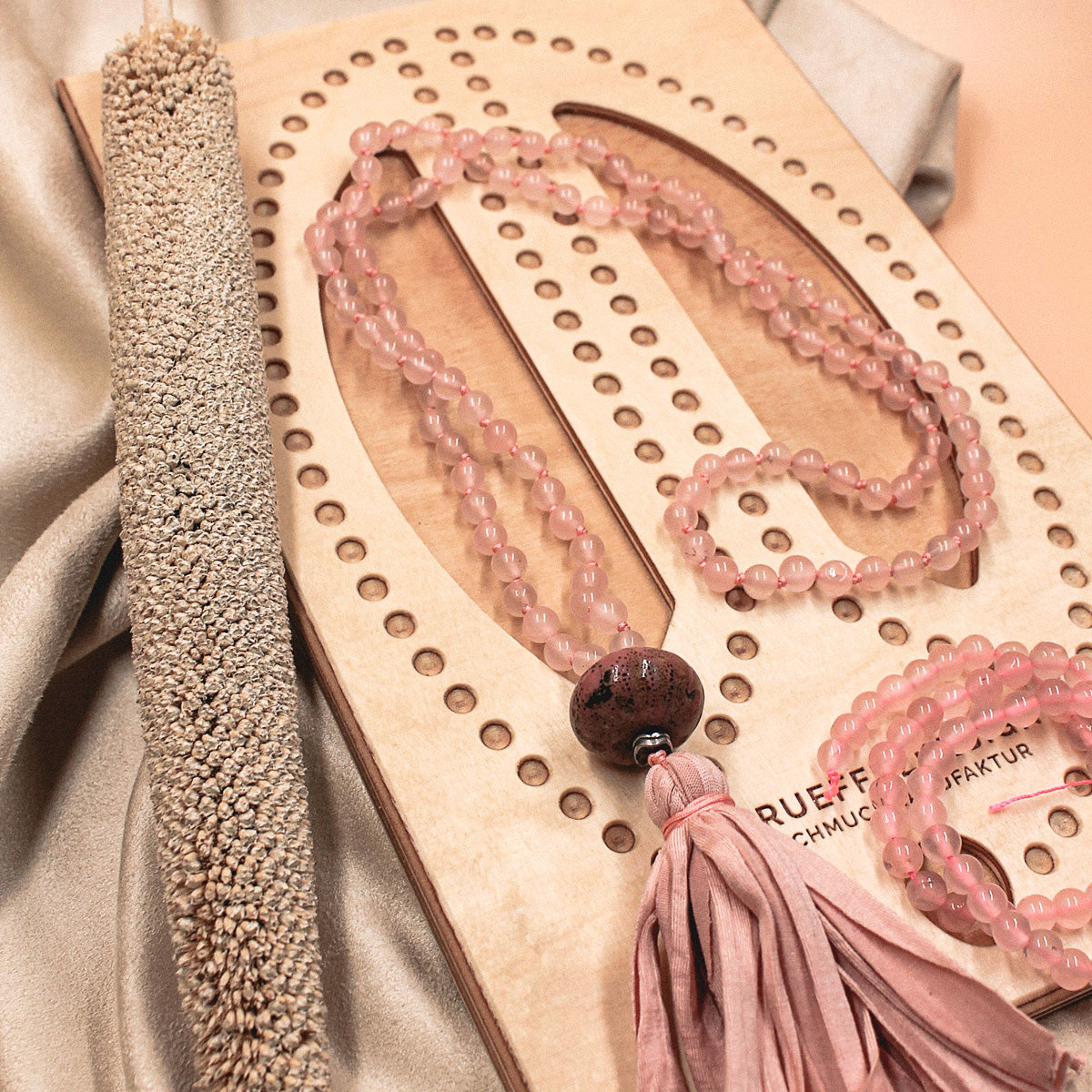 Rosa Mala-Kette mit Quaste liegt auf Holzbrett für Schmuckherstellung