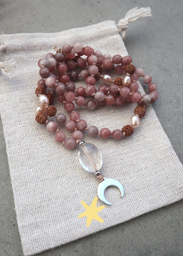 Mala Kette aus Sonnenstein, Rudraksha-Perlen und einem silbernen Mondanhänger aus Edelstahl auf einem Stoffsäckchen.