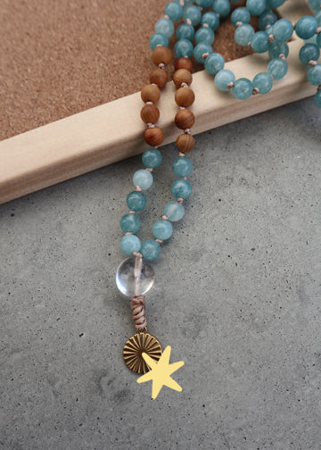 Handgefertigte Mala Kette aus blauem Aquamarin, duftendem Sandelholz und einem runden Sonnen-Anhänger aus Edelstahl