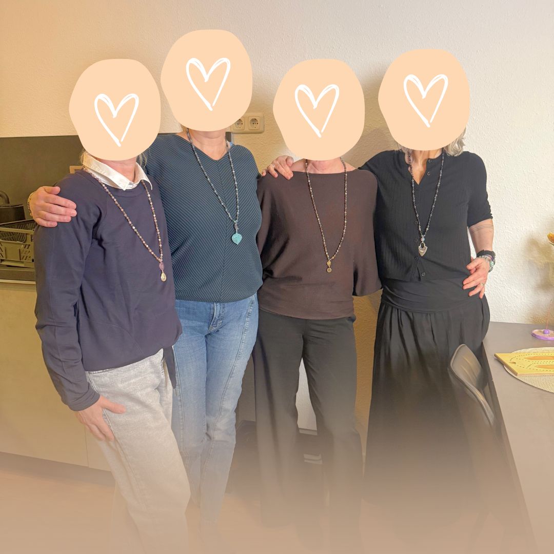 Eine Gruppe glücklicher Frauen präsentiert stolz ihre selbstgemachten Edelstein-Malas nach dem Workshop.