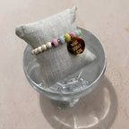 Mantra Armband Gold mit pastellfarbenen Perlen auf grauem Schmuckkissen – Produktfoto wasserfester Schmuck
