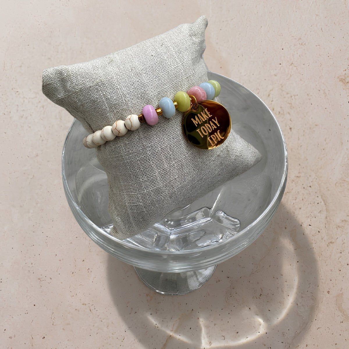 Mantra Armband Gold mit pastellfarbenen Perlen auf grauem Schmuckkissen – Produktfoto wasserfester Schmuck