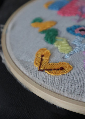 Detailaufnahme von modern embroidery in einem Holzrahmen mit gelben und bunten Garn-Stichen auf hellem Stoff.