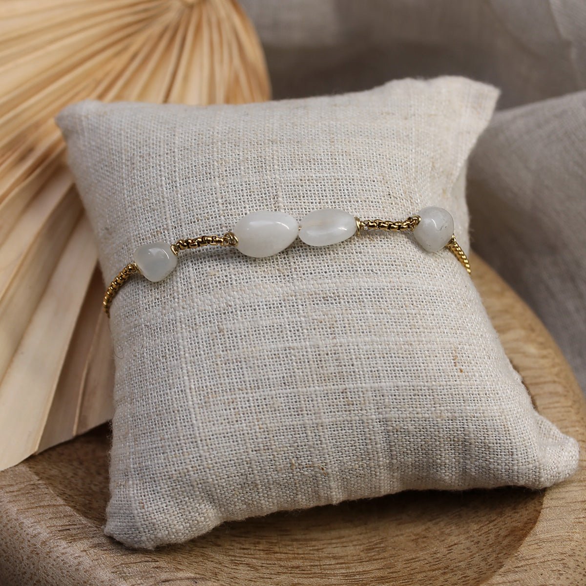 Vergoldetes Mondstein-Armband an einem kleinen cremefarbenen Schmuckkissen präsentiert auf einer Holzschale mit Trockenblume.