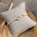 Filigranes Mondstein-Perlenarmband mit vergoldetem Mondanhänger präsentiert auf einem cremefarbenen Schmuckkissen.