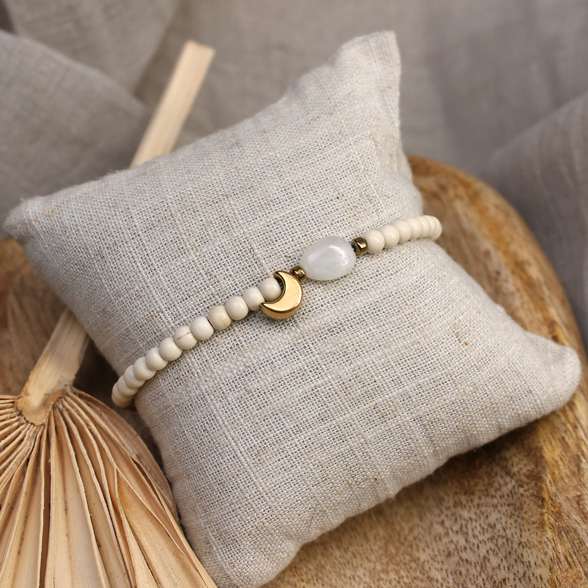 Filigranes Mondstein-Perlenarmband mit vergoldetem Mondanhänger präsentiert auf einem cremefarbenen Schmuckkissen.