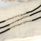 Drei Morsecode Armbänder Selflove aus schwarzen, goldenen und beigen Perlen auf Stoffunterlage