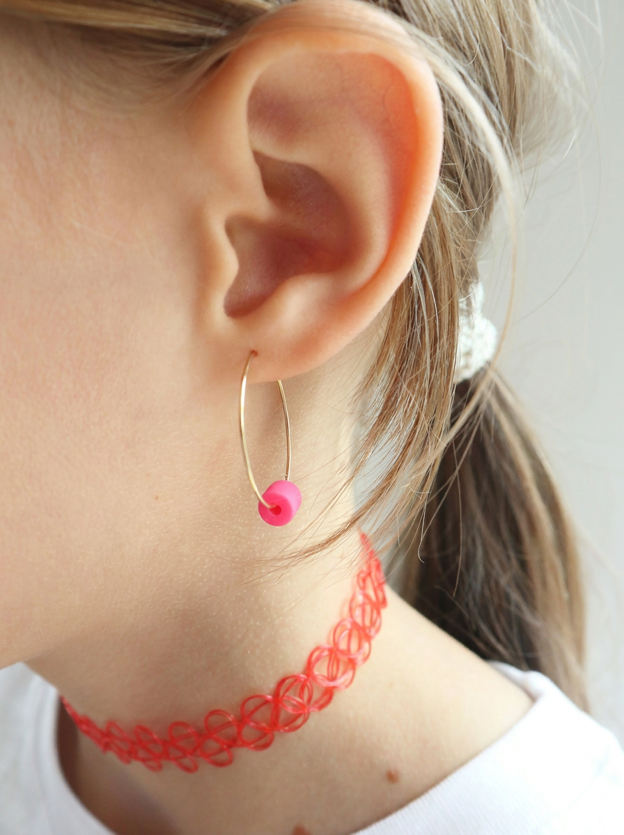 Große goldene Creolen mit pinker Perle, getragen von einem Mädchen mit rotem Tattoo-Choker und weißem Shirt. Trueffeldesign