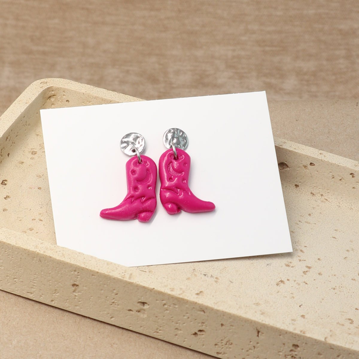 Pinke Cowboy-Boots-Ohrringe liegen auf Schmuckkarte in heller Schmuckschale
