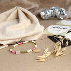 Rosenquarz Armband mit grünen, rosa und weißen Perlen liegt auf einem beigen Untergrund