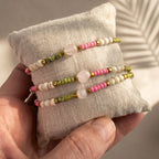 Drei handgefertigte Edelstein-Armbänder mit Rosenquarz-Herz präsentiert auf einem cremefarbenen Leinenkissen mit sanftem Schattenwurf. | trueffeldesign