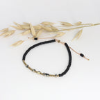Minimalistisches Morsecode Armband Selflove mit schwarzen und goldenen Perlen neben getrockneten Halmen
