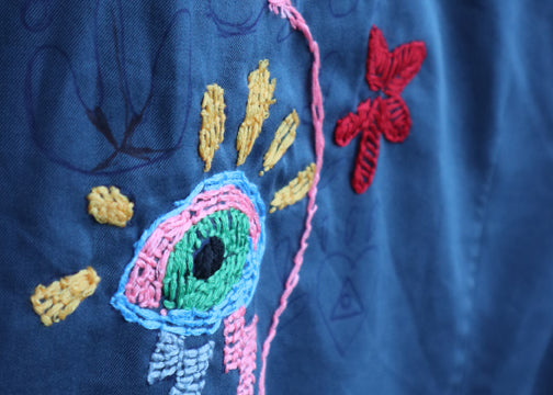 Bunte moderne Stickerei mit einem gestickten Auge als kreatives Kleidungs-Upcycling auf blauem Stoff.