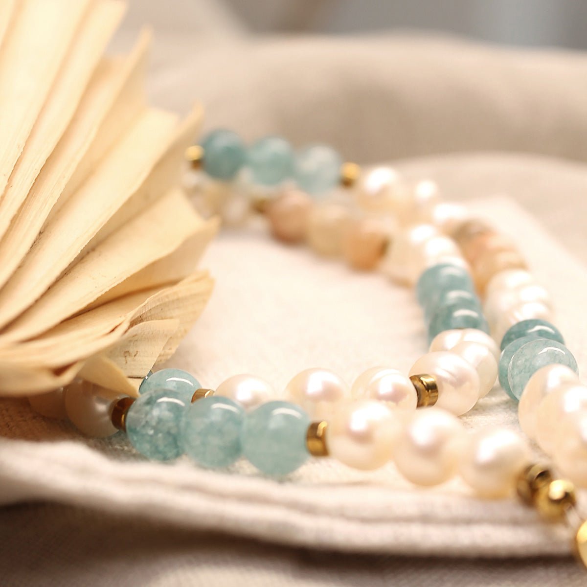 Detaillierte Nahaufnahme der Perlenkette mit Fokus auf die verschiedenen Perlenarten: weiße Upcycling-Süßwasserperlen, hellblaue Aquamarin-Steine und warm-goldene Sonnenstein-Perlen.